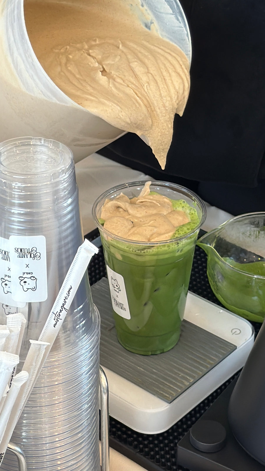 Pouring fig cream foam onto an iced matcha at the Choji x Solante pop-up